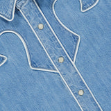 Close-up of The Country Exe’s Shirt by MOTHER, an oversized denim shirt featuring white piping details, silver snap buttons, and a pointed collar. Decorative stitching forms a western-inspired pattern on the front, channeling the timeless charm of a classic cowboy shirt.