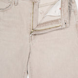 A close-up of The Dodger Slouchy Fit Sneak Pants by MOTHER, in light beige denim with a straight leg, open waistband and fly revealing a gold zipper and white pocket lining, laid flat on a white background.
