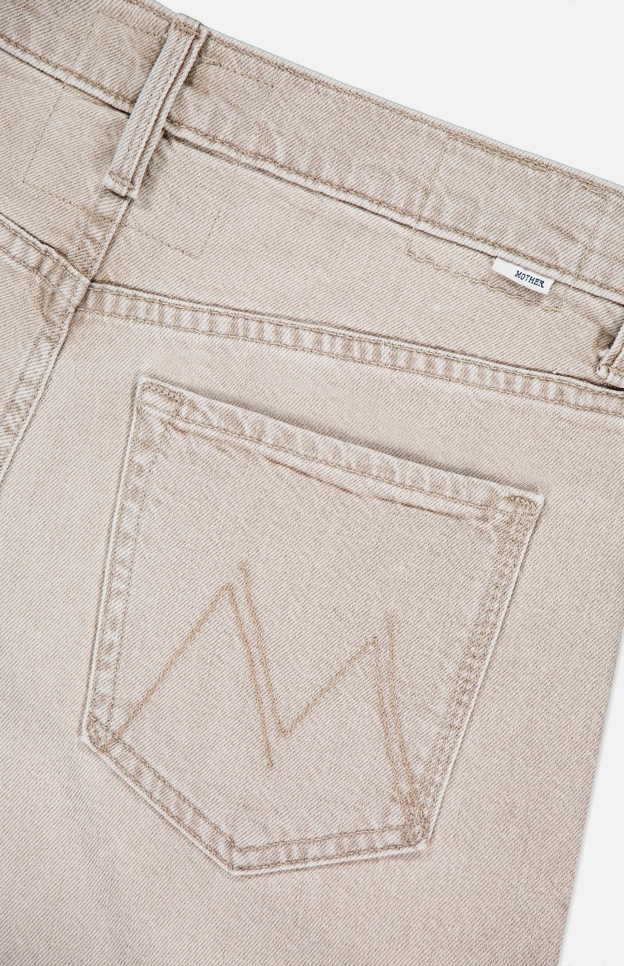 Close-up of the back of MOTHER's The Dodger Slouchy Fit Sneak Pants in light beige denim, featuring a single rear pocket with an M-shaped stitch and a small white label near the waistband.