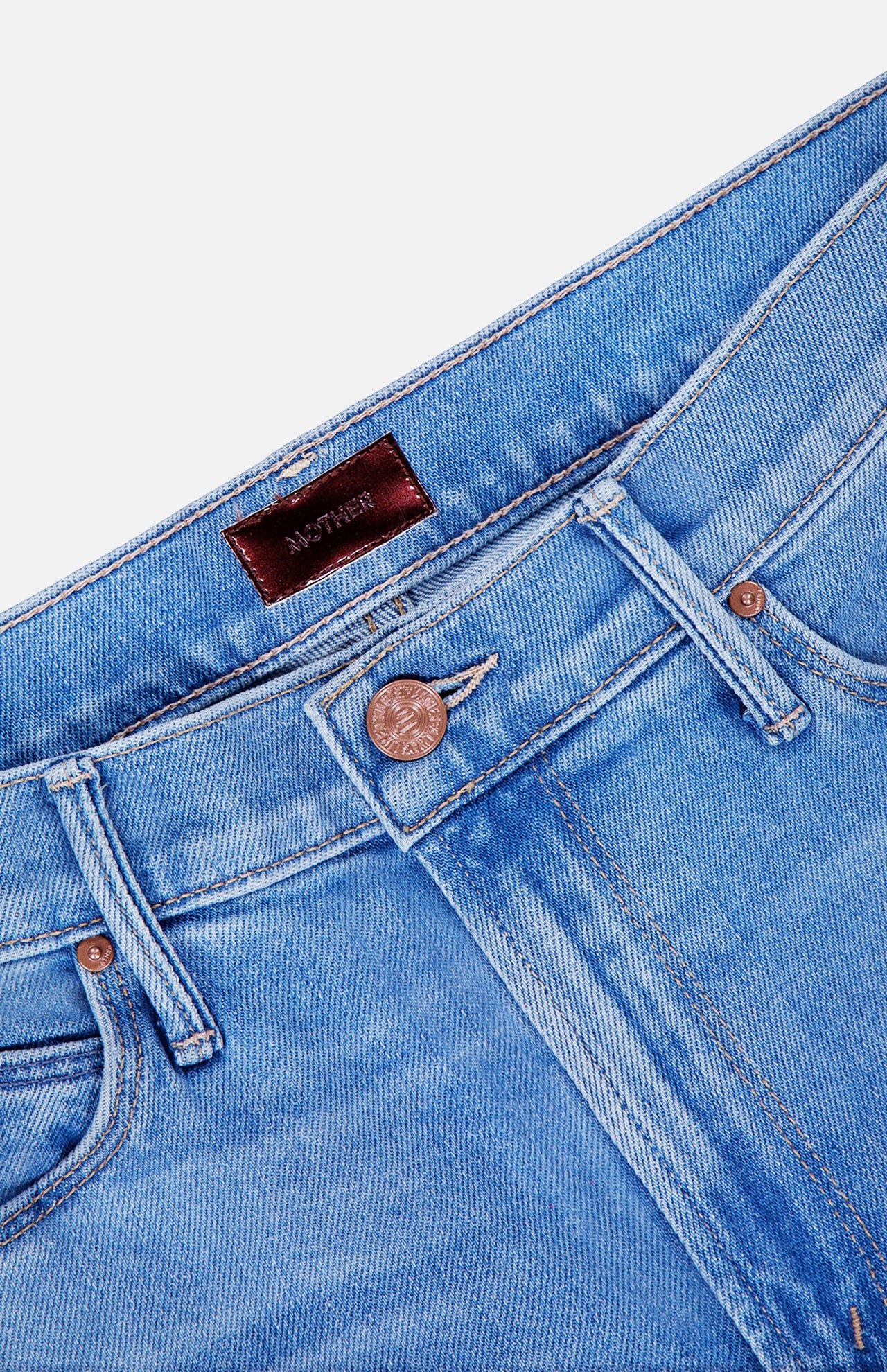 Close-up of The Doozy Jean in Room Service by MOTHER, highlighting the blue denim waistband, copper button, belt loops, front pockets, and a brown leather brand patch on the inner waistband.