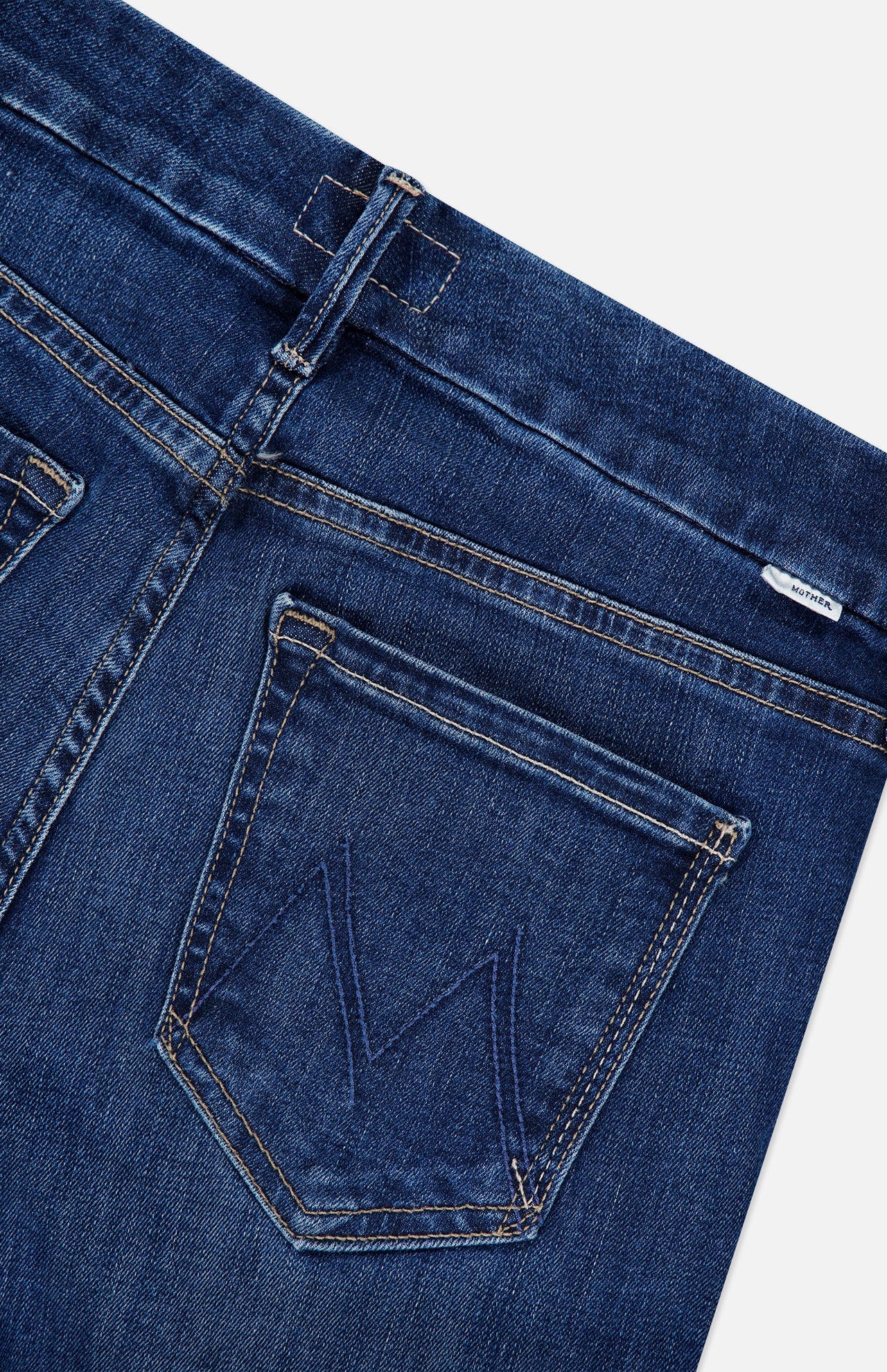 Close-up of the back of dark blue stretch Mother The Down Low Looker Hover Jeans in Backstage, featuring a back pocket with a stitched M logo and a small logo tag at the waistband.