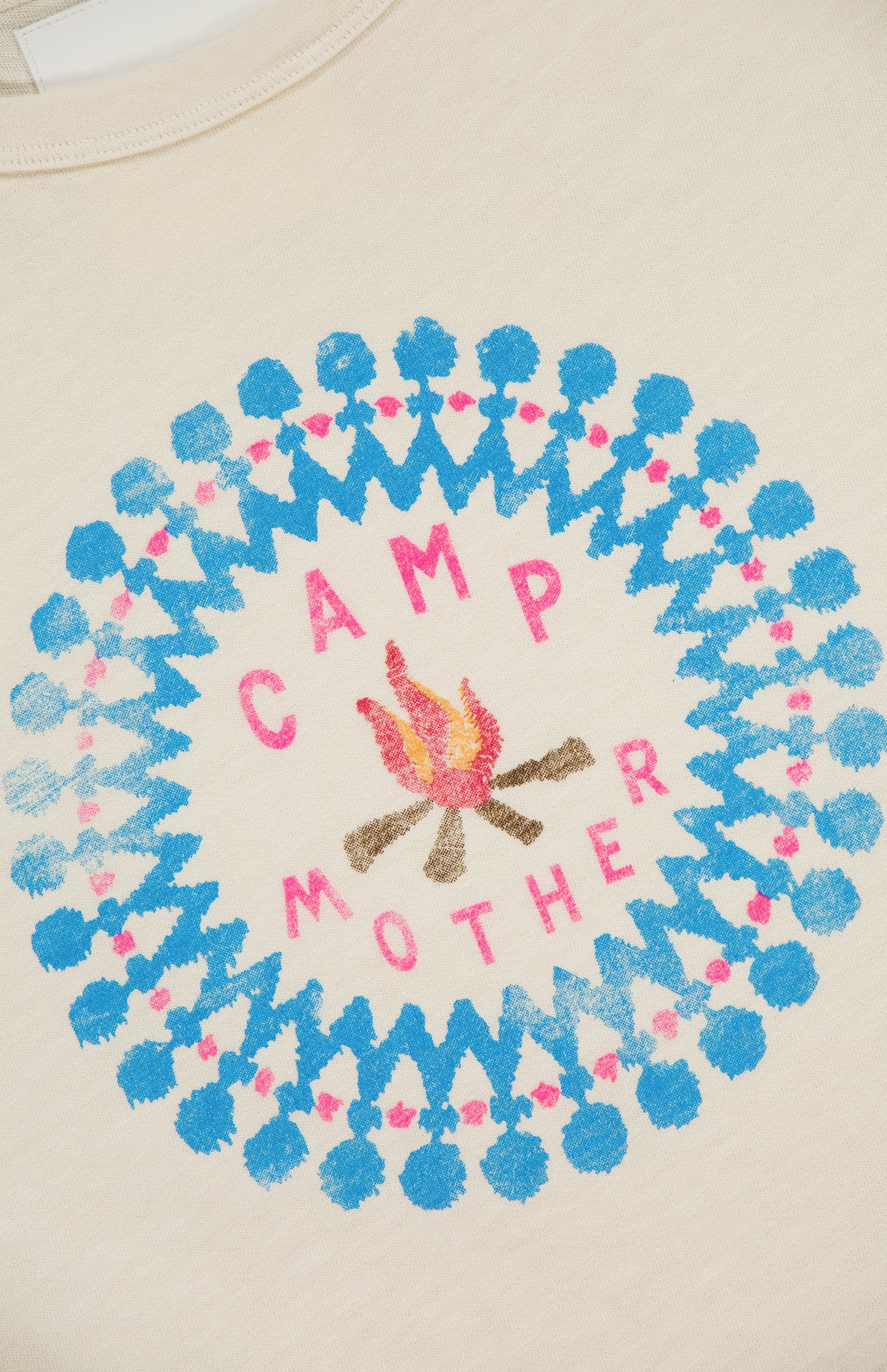 The Flirt Squad Tank Top by MOTHER is an off-white crew neck featuring a campfire illustration and colorful CAMP MOTHER design, accented with a blue and pink circular pattern for a vintage-inspired look.