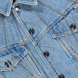 Close-up of the MOTHER Rhinestone Fringe Fly Away Jacket in light blue denim, adorned with decorative silver studs, metallic chain embellishments, and dazzling rhinestone fringe. Featuring metal buttons and detailed stitching, this jacket is the perfect statement piece for any party.
