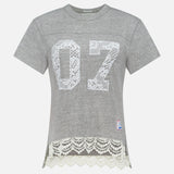 The Footballer Lace T-shirt by MOTHER is a sporty, boxy-fit gray short-sleeve tee with a white lace “07” on the front, lace hem trim, and a small patch—perfect for channeling football jersey vibes.