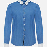 The Frilly Foxy Boxy Denim Shirt by MOTHER is a 100% cotton button-down with long sleeves, white scalloped trim on the collar and cuffs, and detailed white embroidered accents for a chic touch.