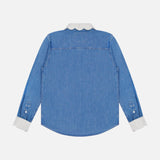 The Frilly Foxy Boxy Denim Shirt by MOTHER is a blue long-sleeve button-down with a white scalloped collar, cuffs, and delicate white trim embroidery, shown from the back on a plain white background.
