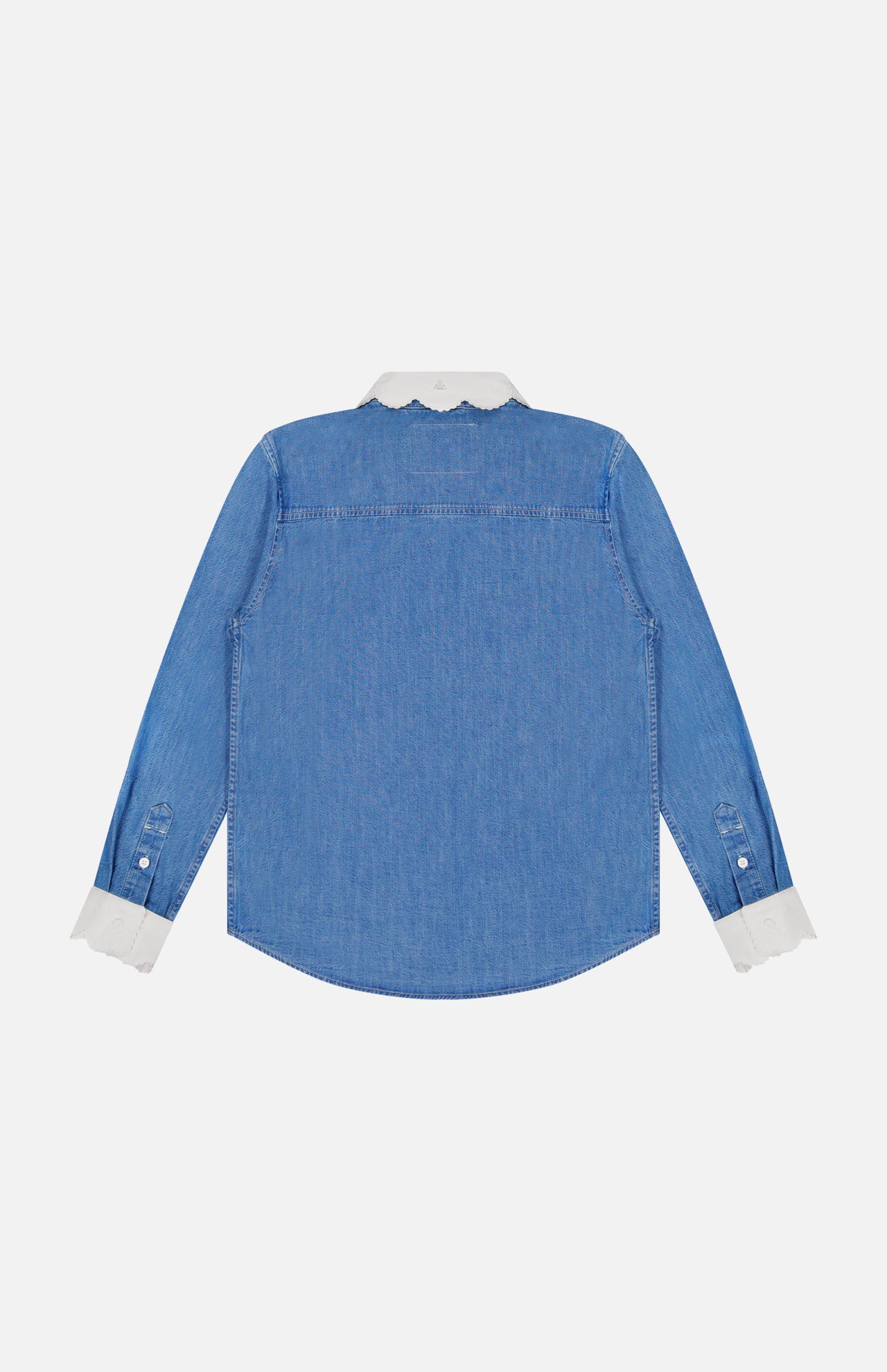 The Frilly Foxy Boxy Denim Shirt by MOTHER is a blue long-sleeve button-down with a white scalloped collar, cuffs, and delicate white trim embroidery, shown from the back on a plain white background.