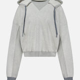 The Half Base Hoodie Sweatshirt by MOTHER features a light gray color, V-neck design, and is accented with dark gray drawstrings along with matching ribbed cuffs and hem. Crafted from soft fleece-lined cotton, this oversized hoodie offers a relaxed fit with long sleeves and is showcased against a plain white background.