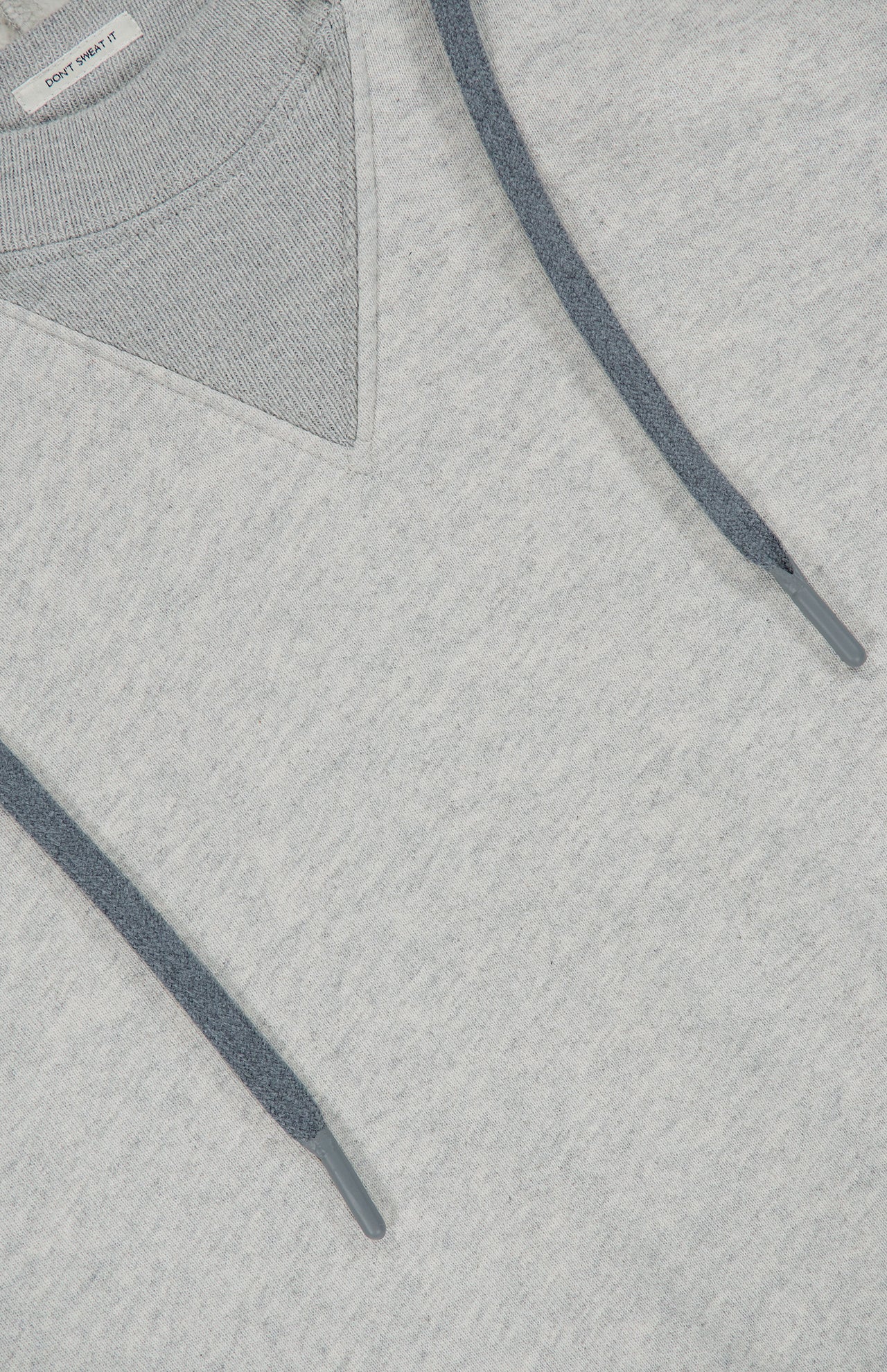 Close-up of The Half Base Hoodie Sweatshirt by MOTHER in light grey, highlighting the drawstrings and V-shaped stitch detail near the neckline. The fleece-lined cotton fabric appears soft and textured, ensuring added comfort.