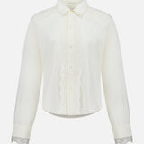 The Headup Honey Shirt by MOTHER is a white long-sleeve blouse with lace trim along the button placket and cuffs, featuring a classic collar and button-down front that combines timeless elegance with subtle western-inspired detailing, displayed on a plain white background.