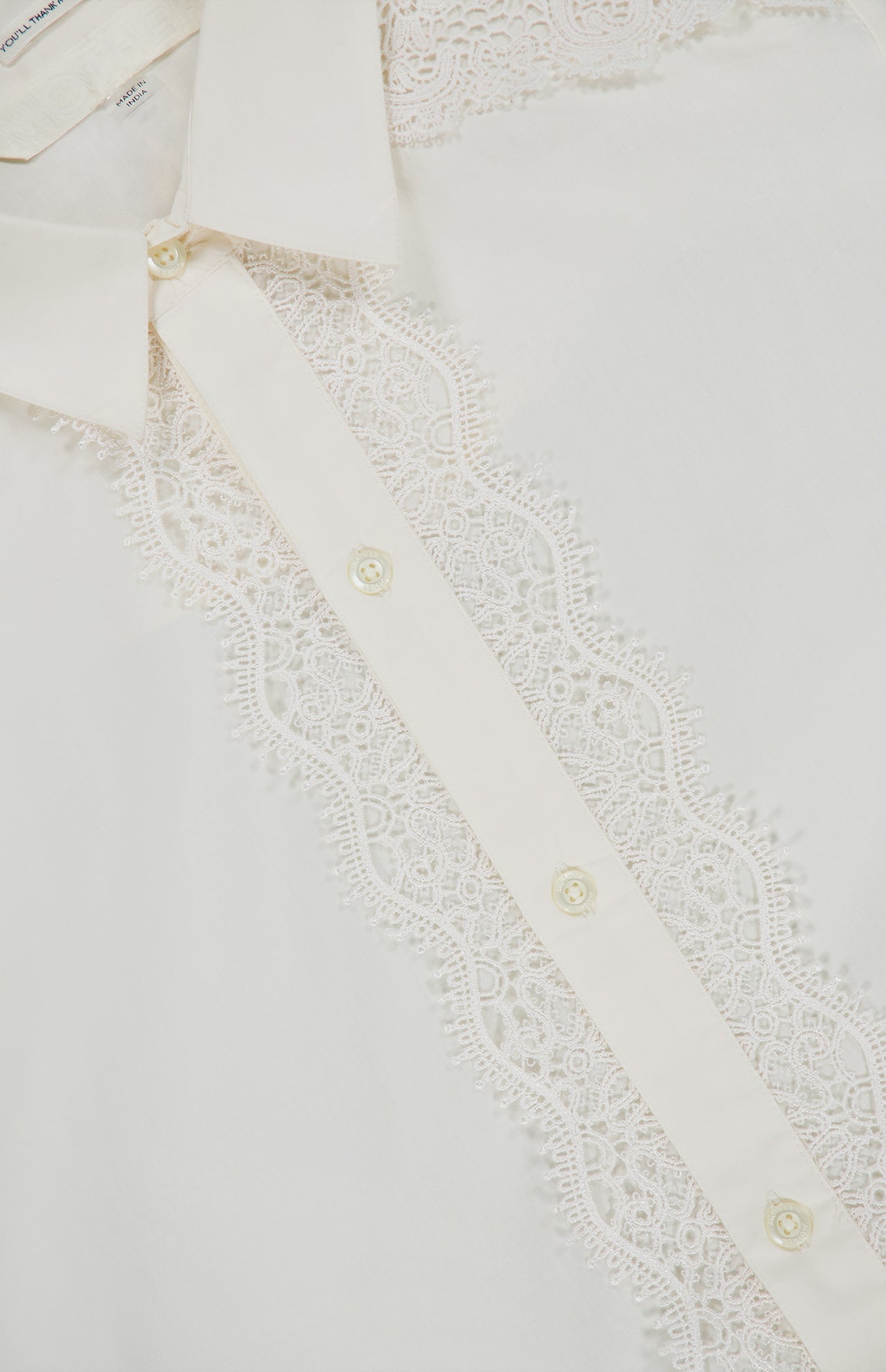 Close-up of MOTHER’s The Headup Honey Shirt, a white, western-inspired design showcasing a vertical panel of intricate lace trim along the button line, with pearl-like buttons and the delicate texture of the fabric visible.