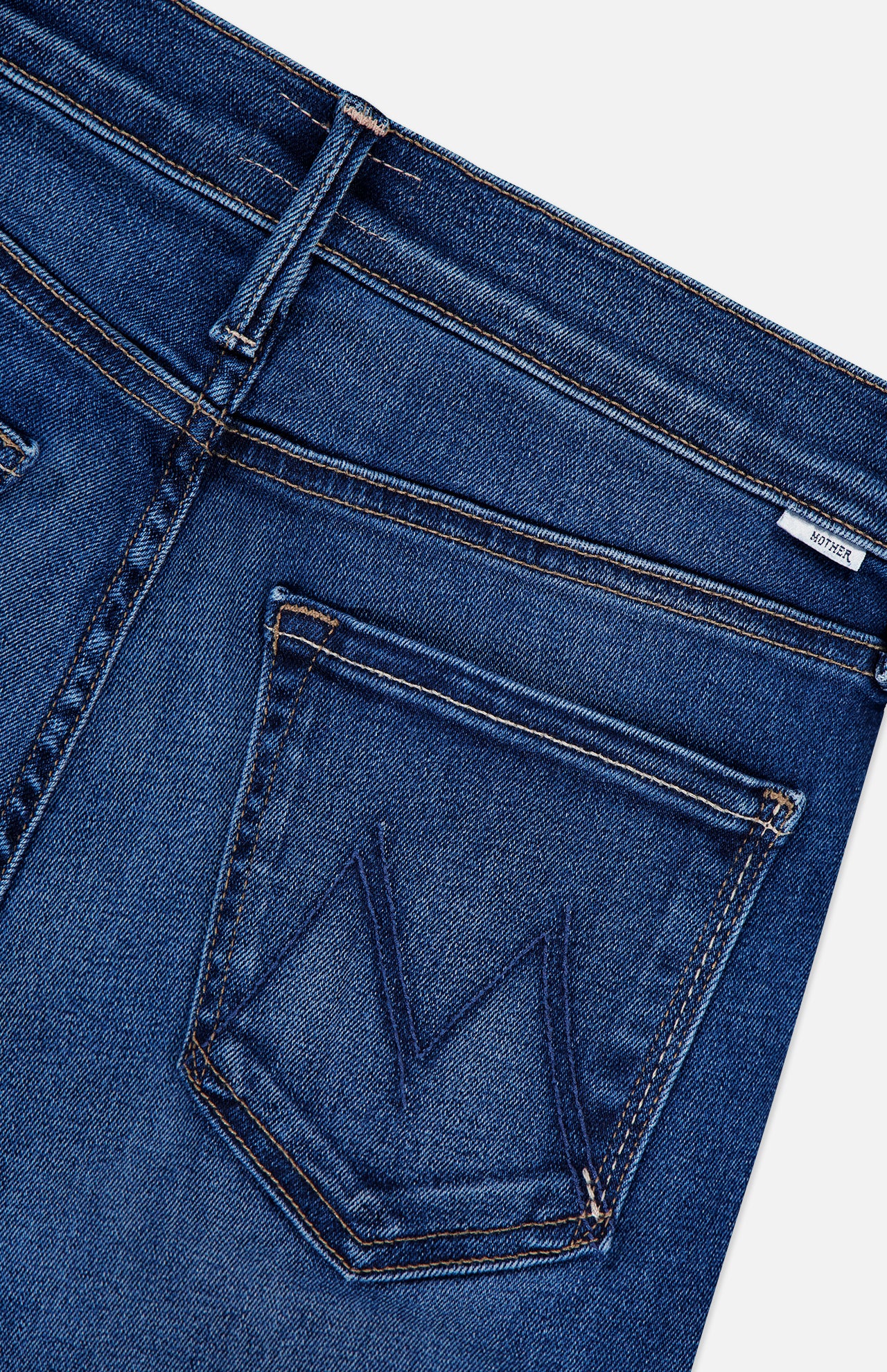 Close-up of the back pocket on MOTHER's The Insider Skimp Jean in Taking Chances, a blue stretch denim style with high waist, bootcut leg, stitched M detail, and vintage-inspired fabric label on the waistband.