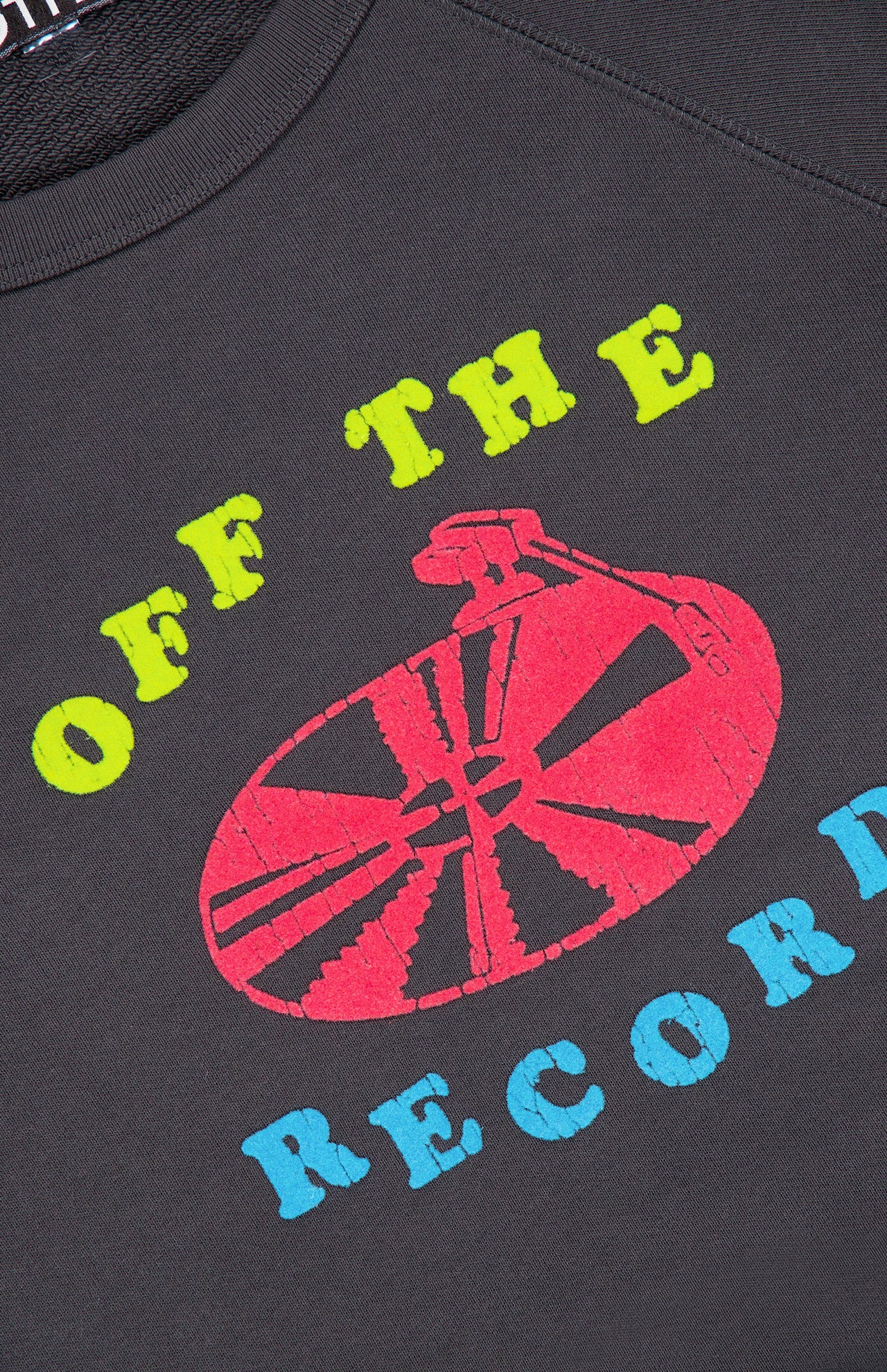The Itty Concert Crewneck Sweatshirt by Mother is a dark gray cropped raglan sweatshirt featuring a lime green and blue OFF THE RECORD graphic with a red illustration of a record player tonearm.