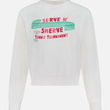 The Itty Concert Tennis Sweater by MOTHER is a white 100% cotton cropped raglan sweatshirt with "SERVE N SWERVE TENNIS TOURNAMENT" in red and green, plus bold net, ball, and racket graphics above the text.