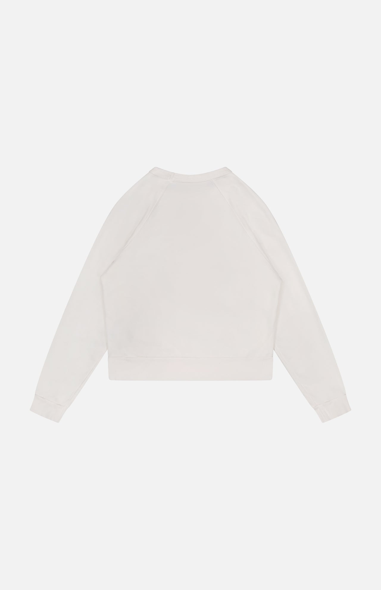 The Itty Concert Tennis Sweater by MOTHER is shown laid flat on a white background, featuring a plain, long-sleeved design in light beige 100% cotton with a back view and no visible logos or designs.