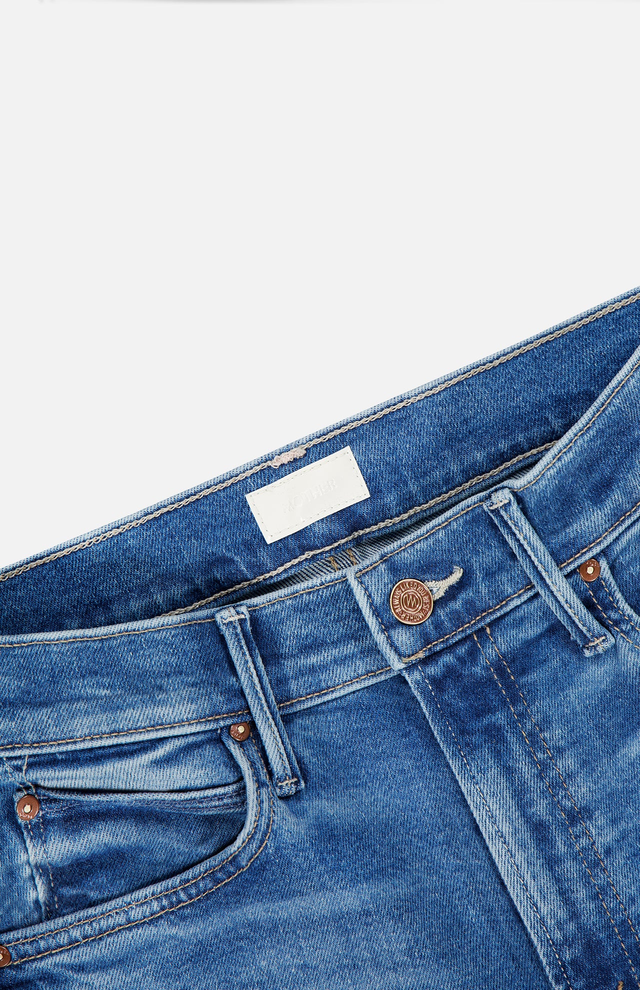 A close-up of the waistband and upper portion of MOTHER’s The Kick It Straight Leg Jean in Bitchin', a high-rise, mid-blue style, highlights the button, belt loops, front pockets, and a blank white label inside.