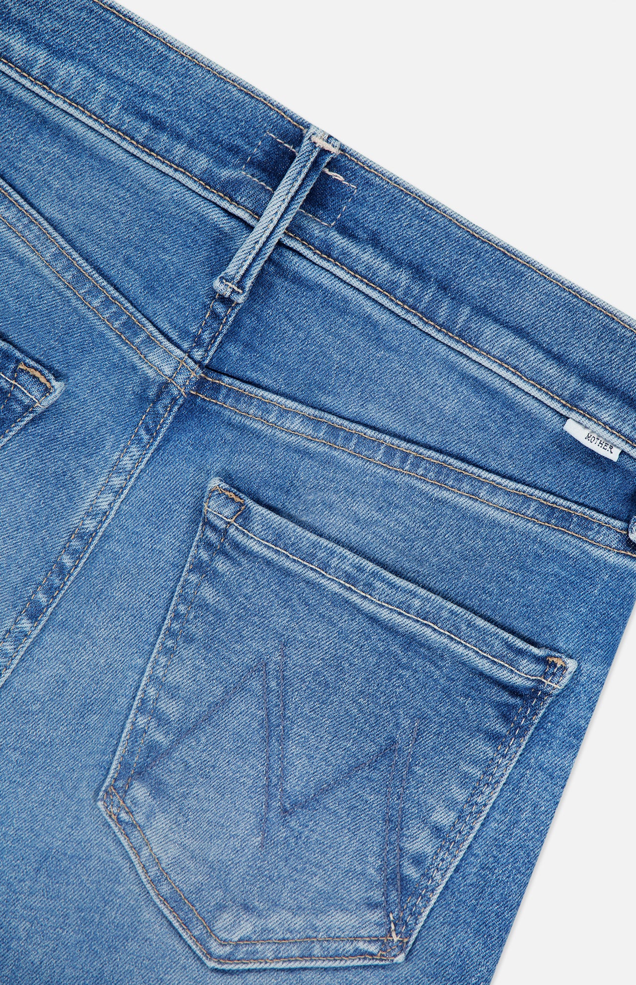 Close-up of the back pocket on MOTHER’s The Kick It Straight Leg Jean in Bitchin’ mid-blue wash, featuring a stitched M detail and part of the waistband with a belt loop.
