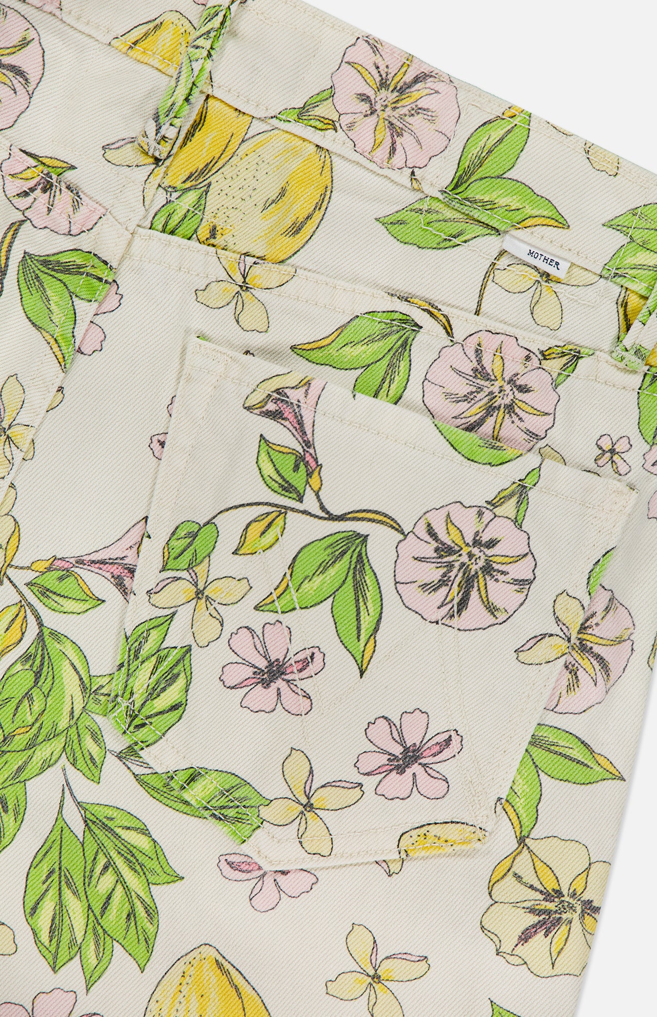 Close-up of the fabric pocket on MOTHER’s The Kick It Pant in Lemonade Stand, a high-rise straight leg denim featuring a cream pastel lemon blossom print with lemons, green leaves, pink flowers, and a small white MOTHER tag near the waistband.
