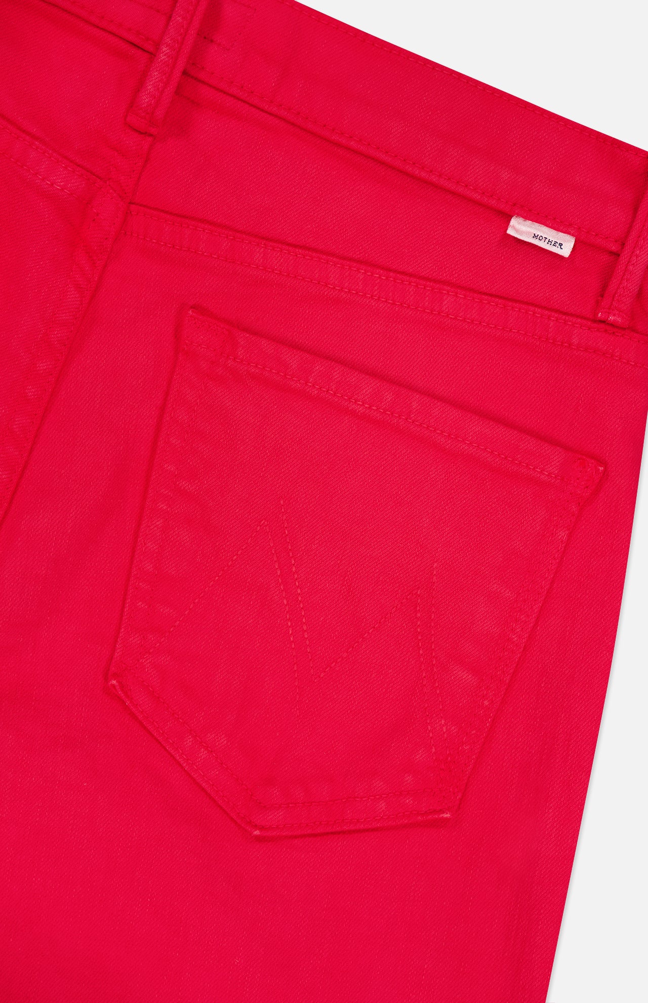 Close-up of The Kick It Pant in Tango Red by MOTHER, showcasing the bright red fabric, a back pocket with visible stitching, and a small white tag with red text near the waistband.