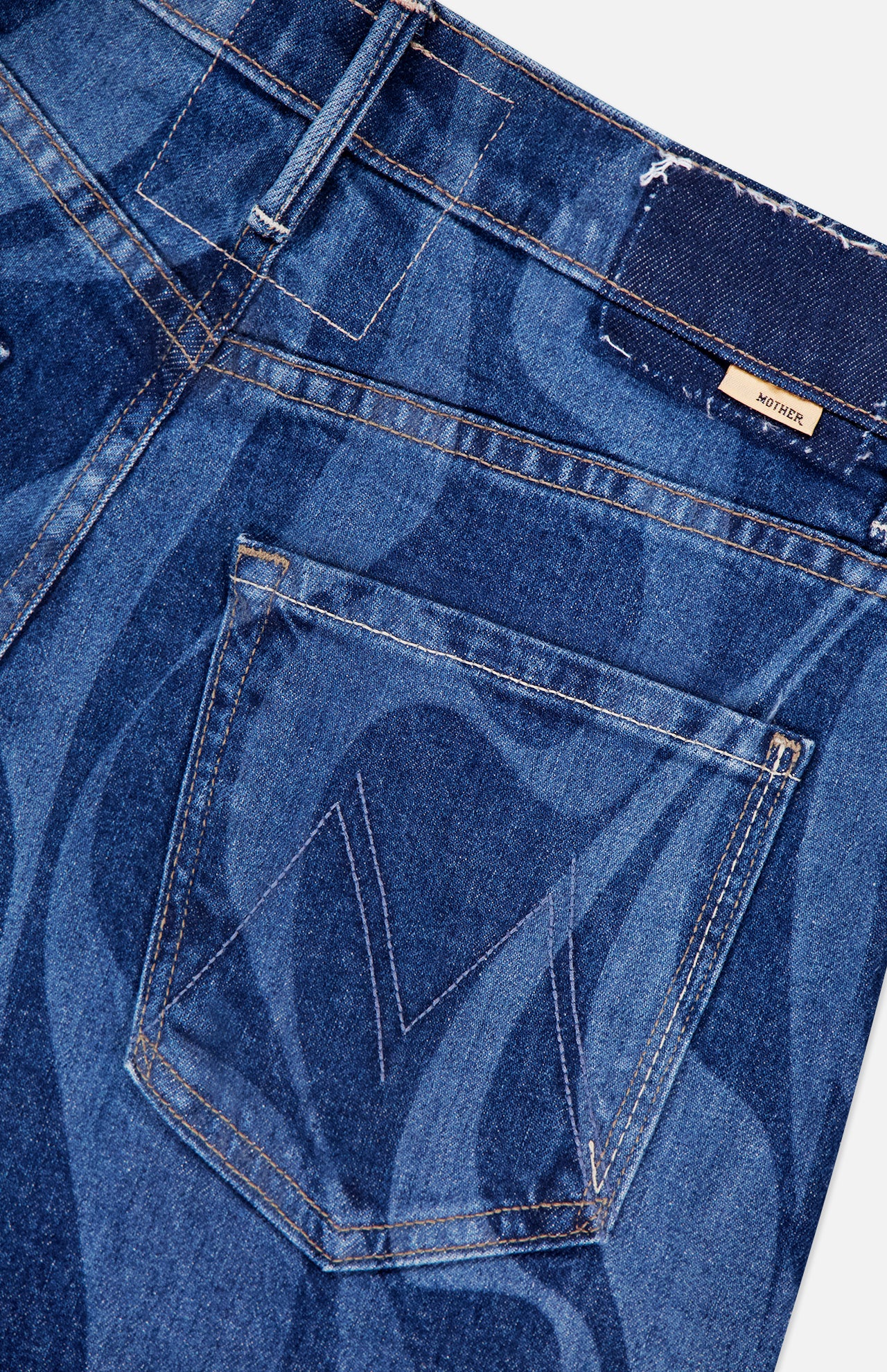 Close-up of The Lasso Sneak Abstract Print Jean by MOTHER, featuring abstract stripes, a stitched back pocket with a subtle M detail, belt loops, and a dark waistband adorned with a small rectangular brand label.