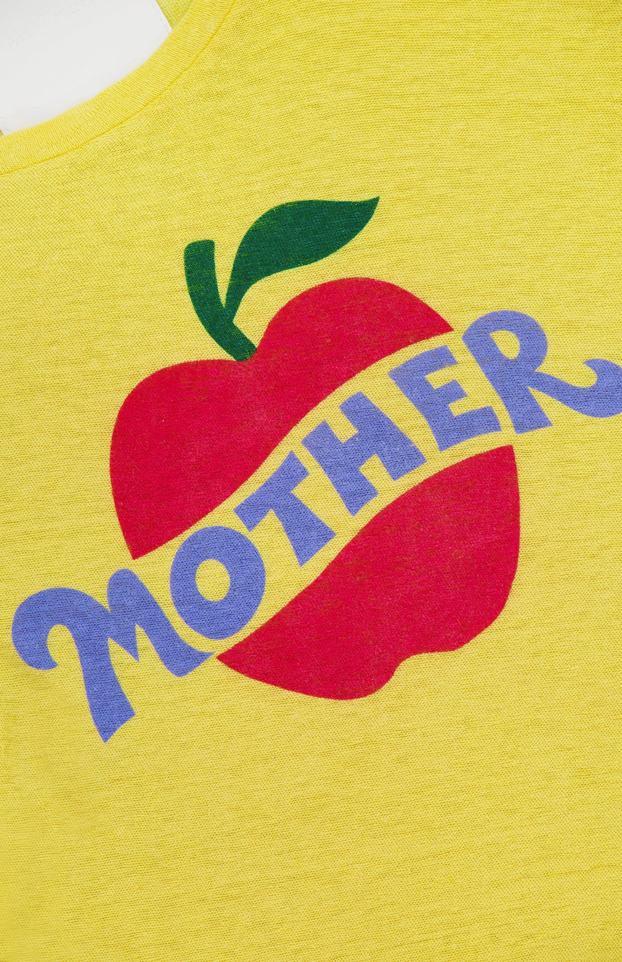 The Lil Sinful Apple T-shirt by MOTHER features a red apple with a green leaf on yellow cotton-linen blend fabric, with "MOTHER" in bold, wavy purple letters diagonally across the apple for a vintage vibe.
