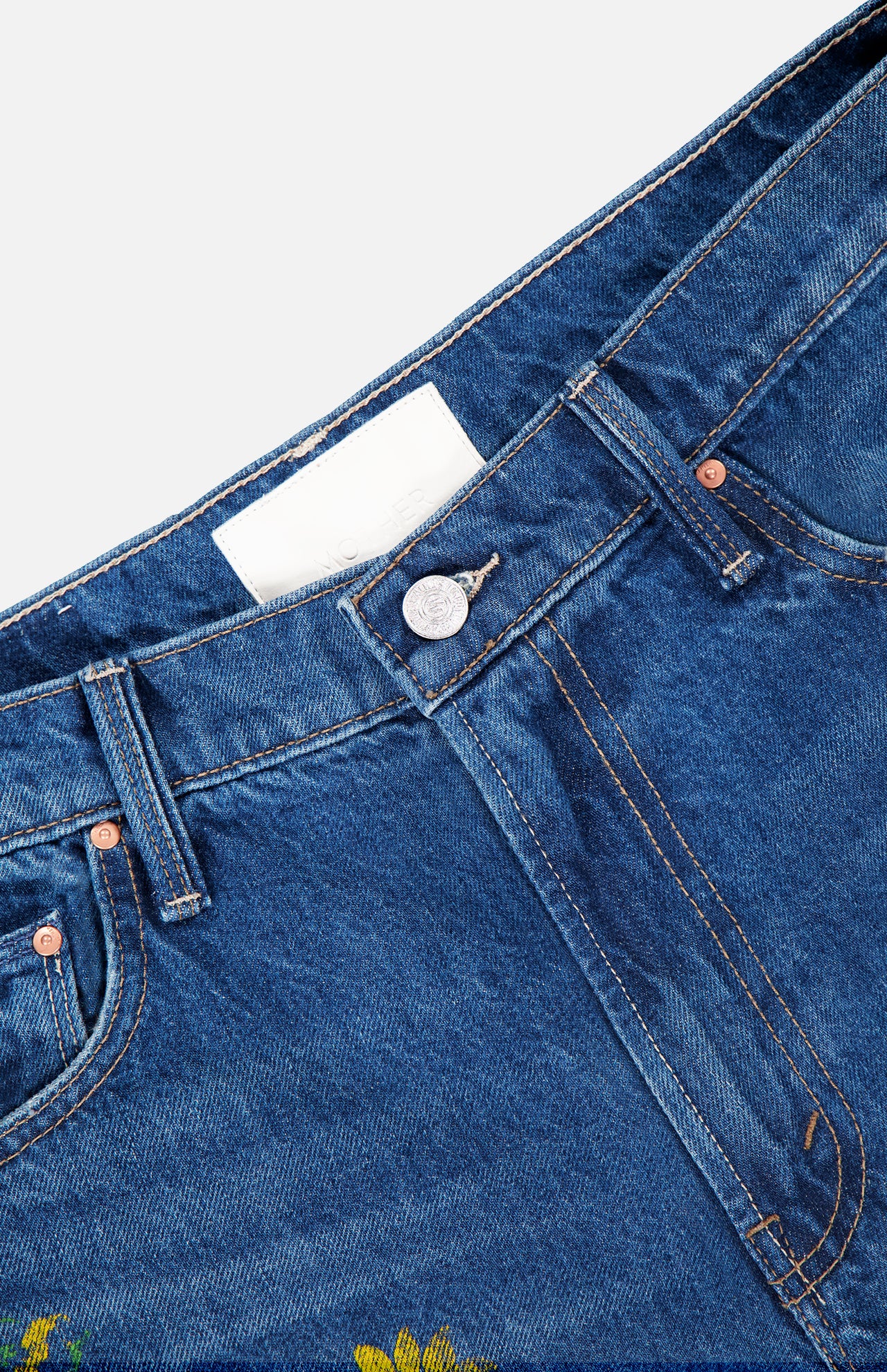 Close-up of the waistband and upper front of MOTHER The Rerun Zip Sneak Floral Print Jeans, featuring a metal button, front pockets, orange stitching, and a blank white label inside.