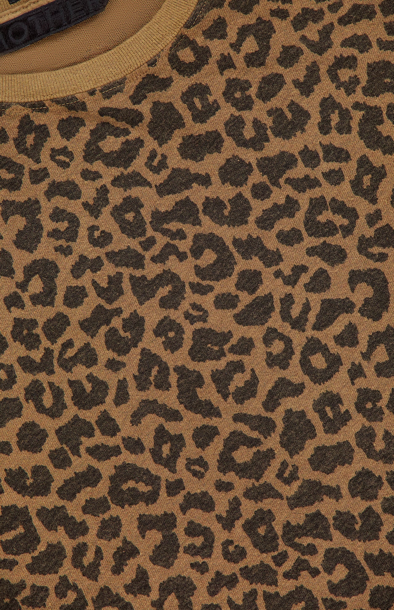 Close-up of brown cotton linen blend fabric with a black cheetah print pattern from The Short Sleeve Boxy Ringer T-shirt by MOTHER, showing part of a round neckline and a clothing label at the top edge.