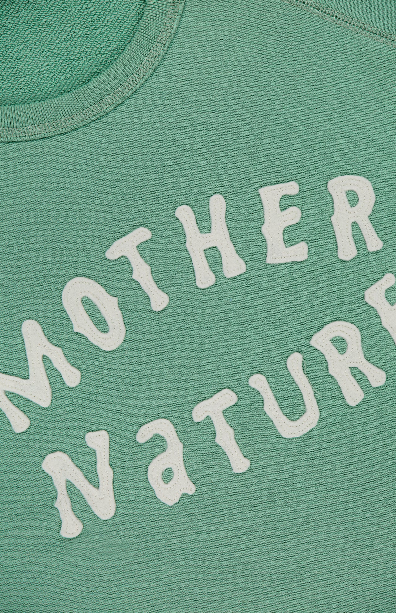 Close-up of The Short Sleeve Concert Shirt by MOTHER, a green 100% cotton raglan sweatshirt featuring raised white "MOTHER NATURE" lettering in a playful, wavy arc across the fabric.