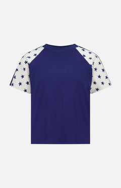 The Concert Race T-shirt by MOTHER is a 100% cotton raglan tee featuring a solid navy blue back and white sleeves with navy blue stars, inspired by classic Americana style. Shown against a plain white background.
