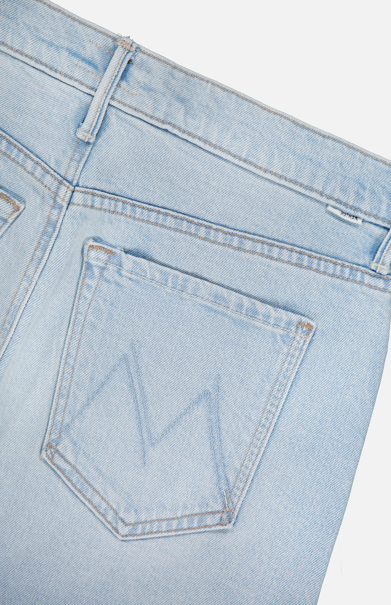 Close-up of the back pocket of MOTHER’s The Vagabond Mini Fray Skirt, a light blue denim style with a stitched M on the pocket, visible waistband and belt loop, plus a subtle frayed hem.