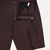 Close-up of NN07 Billie Drawstring Shorts in dark brown linen-viscose, featuring an elastic waistband, drawstring, partially open zipper fly revealing black lining and a small white tag.