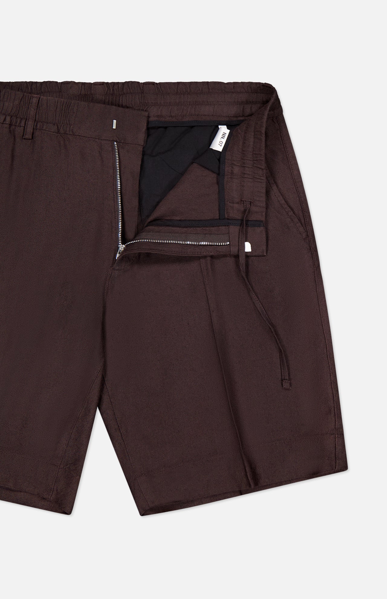 Close-up of NN07 Billie Drawstring Shorts in dark brown linen-viscose, featuring an elastic waistband, drawstring, partially open zipper fly revealing black lining and a small white tag.