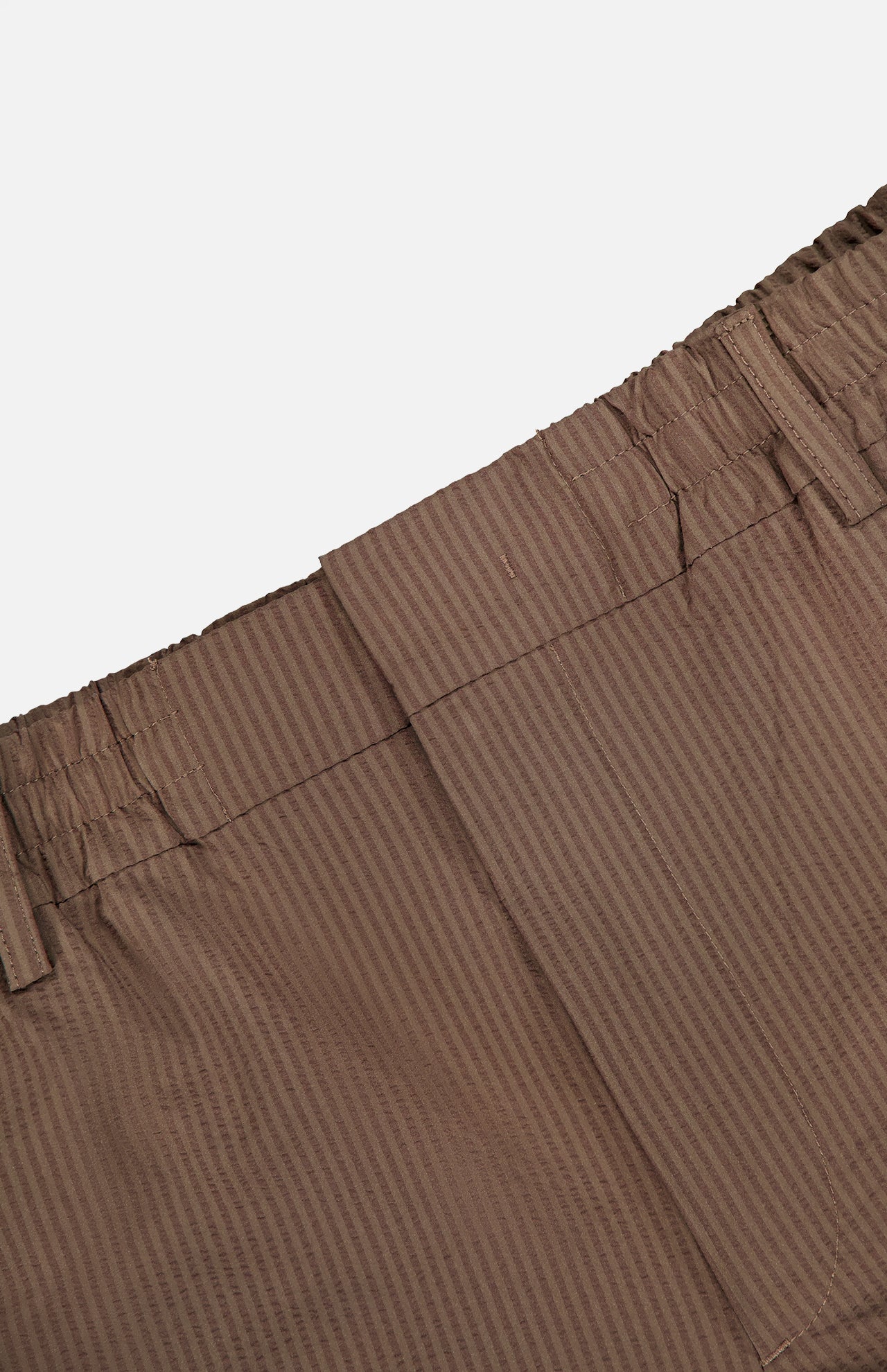 Close-up of the NN07 Billie Seersucker Trouser Pant’s waistband in brown, showcasing subtle vertical stripes, an elasticated waist with belt loops, visible seam detailing, and a clean, minimal finish.