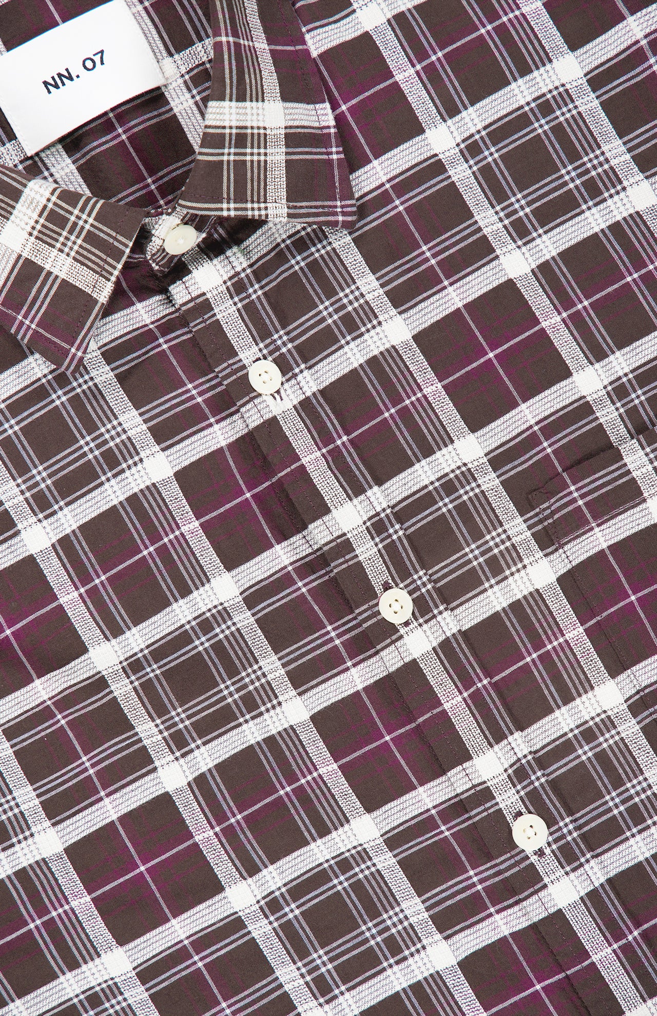 Close-up of the Deon Checkered Long Sleeve Shirt by NN07, featuring a relaxed fit and a brown, white, and purple checked pattern. The shirt collar and a white NN07 label are visible.