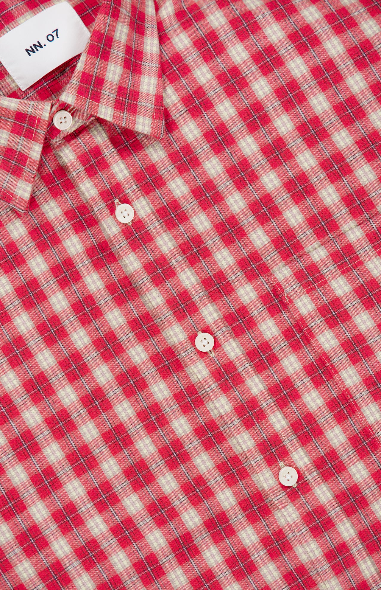 A close-up of the Deon Flannel Long Sleeve Shirt by NN07, showcasing its red and white plaid pattern in organic cotton flannel, detailed with white buttons and a visible NN07 label inside the collar—an essential addition to the modern casual wardrobe.