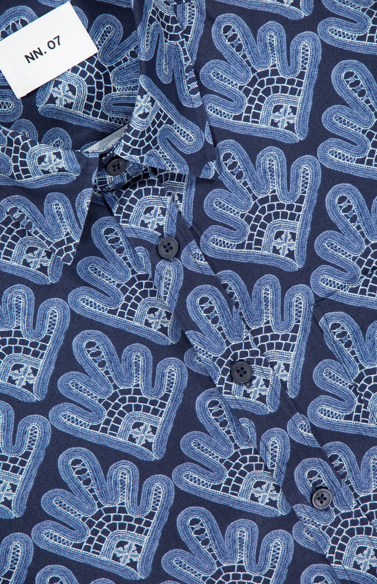 Close-up of the NN07 Deon Short Sleeve Print Shirt in navy blue with abstract light blue hand shapes, dark buttons, and a white NN07 tag on the top left. This modern-casual staple adds style to any wardrobe.