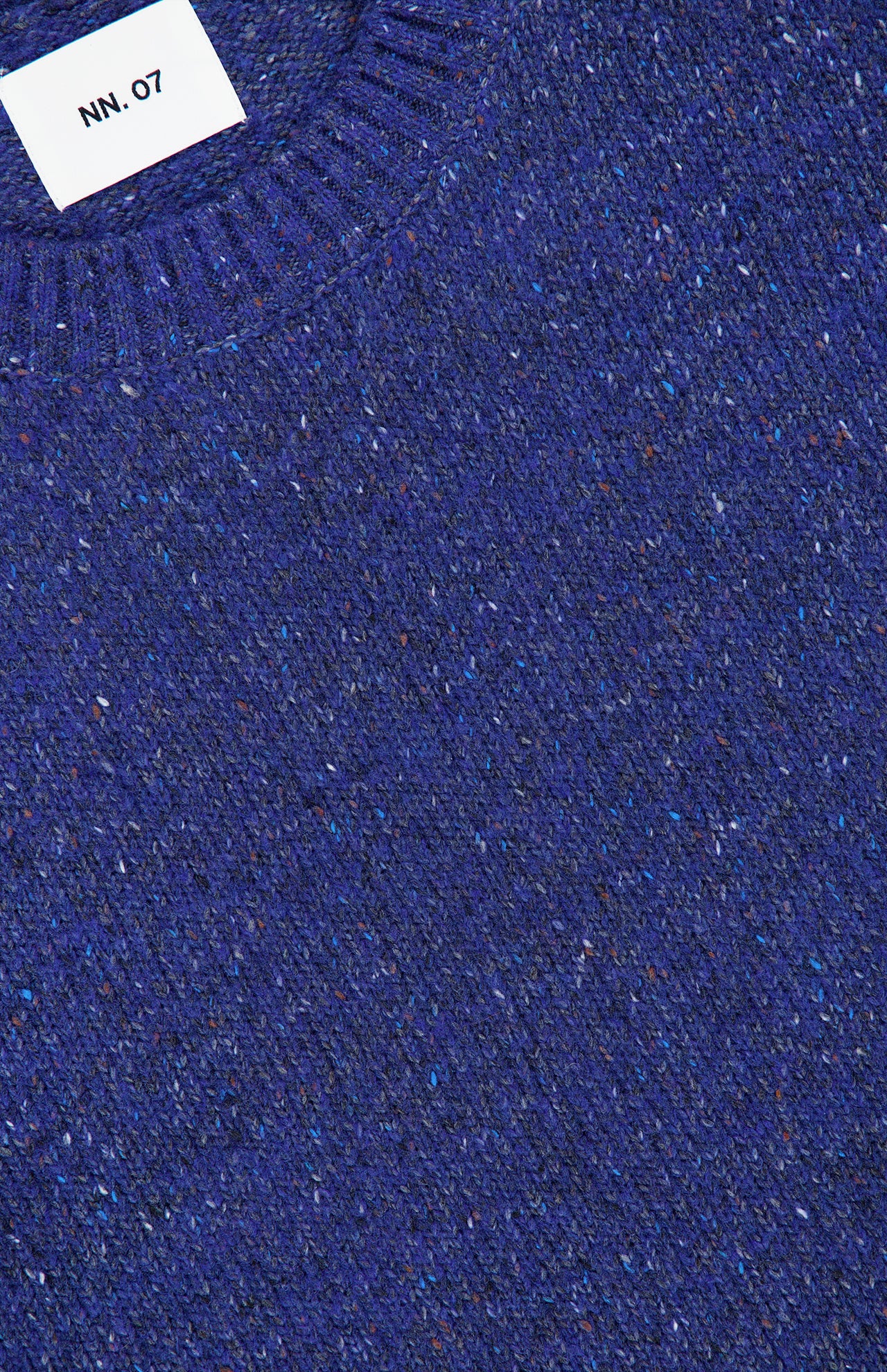 Close-up of the Jim Crew Neck Knitted Sweater by NN07, featuring a textured, speckled bright blue wool-blend jersey knit and a white NN07 label sewn into the ribbed neckline.