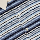 A close-up of the NN07 Nolan Polo Short Sleeve Cardigan Sweater in blue, featuring a white collar, button-down front, and navy and beige horizontal stripes. Crafted from 100% cotton with the NN07 label inside the collar.