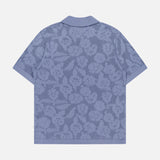 The NN07 Ryan Flower Design Short Sleeve Shirt is a light blue polo made from organic cotton, featuring an all-over flower jacquard pattern, a collar, and shown flat with the back facing up against a white background.