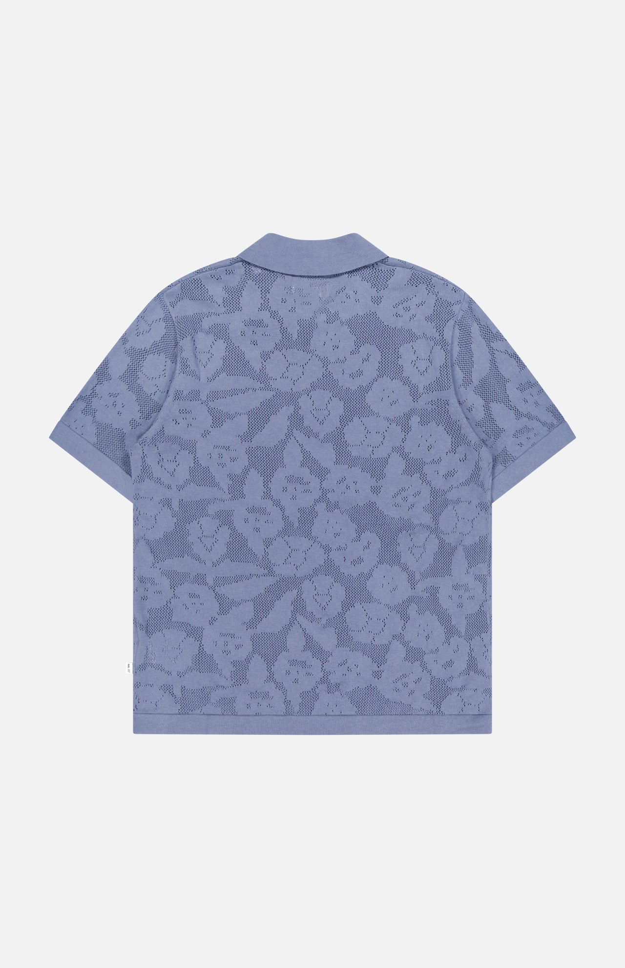 The NN07 Ryan Flower Design Short Sleeve Shirt is a light blue polo made from organic cotton, featuring an all-over flower jacquard pattern, a collar, and shown flat with the back facing up against a white background.