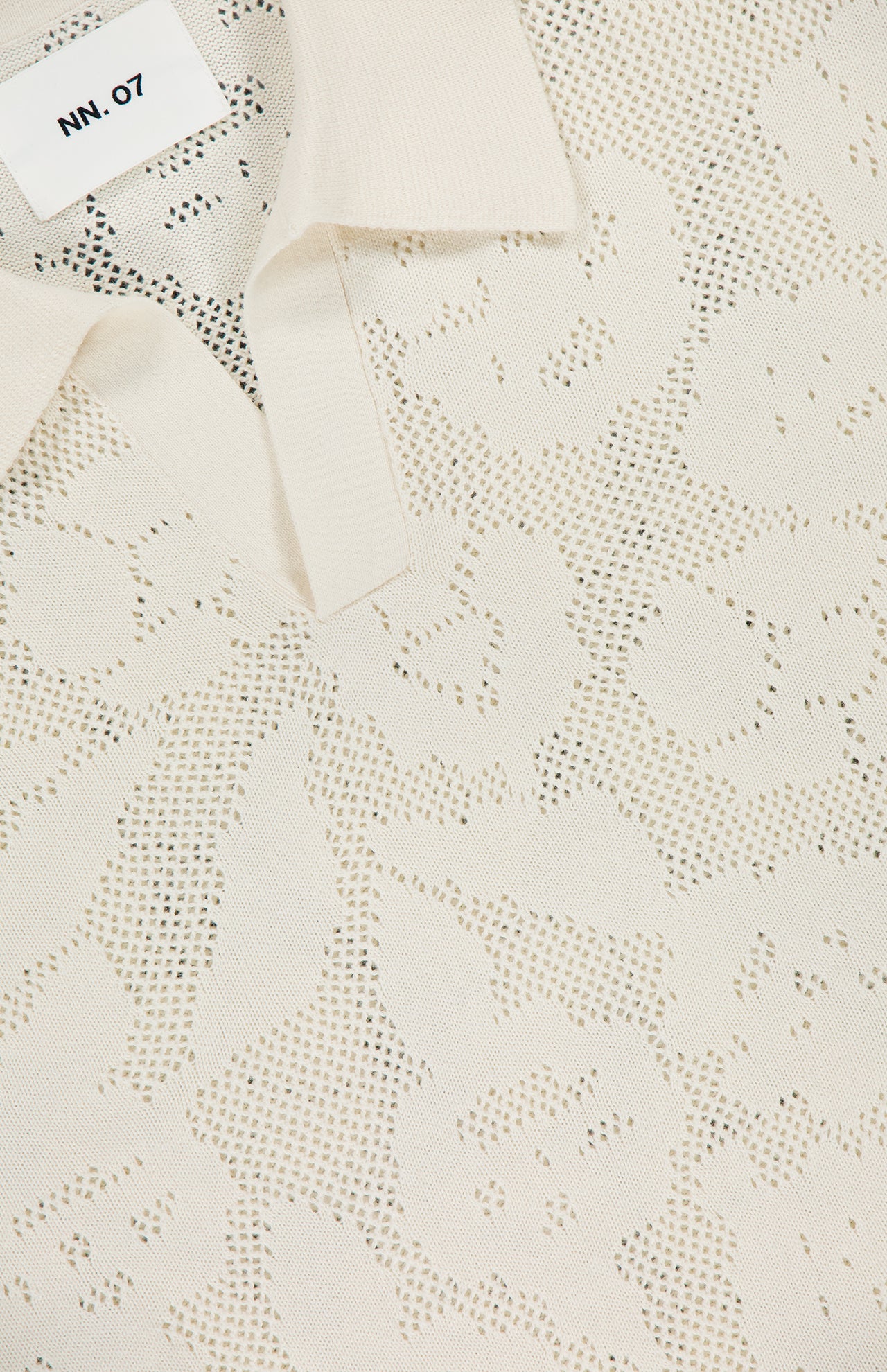 Close-up of the NN07 Ryan Flower Design Short Sleeve Shirt in ivory knit, featuring a subtle jacquard flower pattern and a white NN07 label sewn inside the collar.
