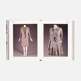 An open book from ASSOULINE’s "Chanel: The Impossible Collection" displays vintage women's suits—one a tailored skirt suit, the other a pleated skirt with matching jacket, both showcasing Chanel’s luxe minimalism in patterned fabrics.