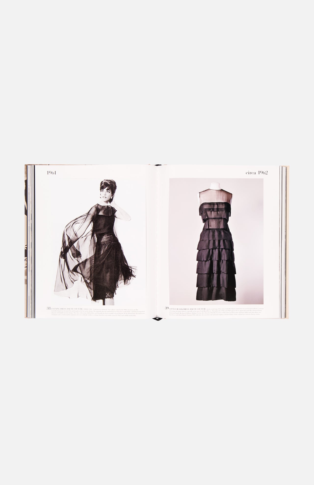 An open book, Chanel: The Impossible Collection by ASSOULINE, displays modern fashion with a woman modeling a black sheer tiered dress on the left and the same dress on a mannequin on the right—both set against luxe white minimalism.