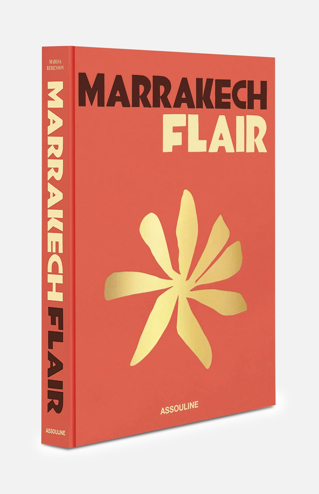 A vibrant red and orange book titled *Marrakech Flair* by ASSOULINE features bold typography and a gold abstract flower on the cover, with the title displayed on both the spine and front, and the ASSOULINE brand name at the bottom.