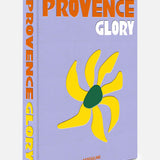 ASSOULINE’s Provence Glory features a lavender cover with bold orange and white lettering, adorned with a yellow abstract sun design with a green center—capturing the vibrant spirit and timeless charm of the South of France.
