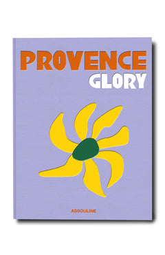 The Provence Glory book cover by ASSOULINE displays bold orange and white text on a lavender background, accented by a simple yellow flower illustration, evoking Mediterranean travel in the South of France.