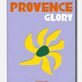 The book cover for *Provence Glory* by ASSOULINE features a lavender background, bold orange and white lettering displaying the title, a stylized yellow flower with a green center inspired by the South of France, and the brand name ASSOULINE in red at the bottom.