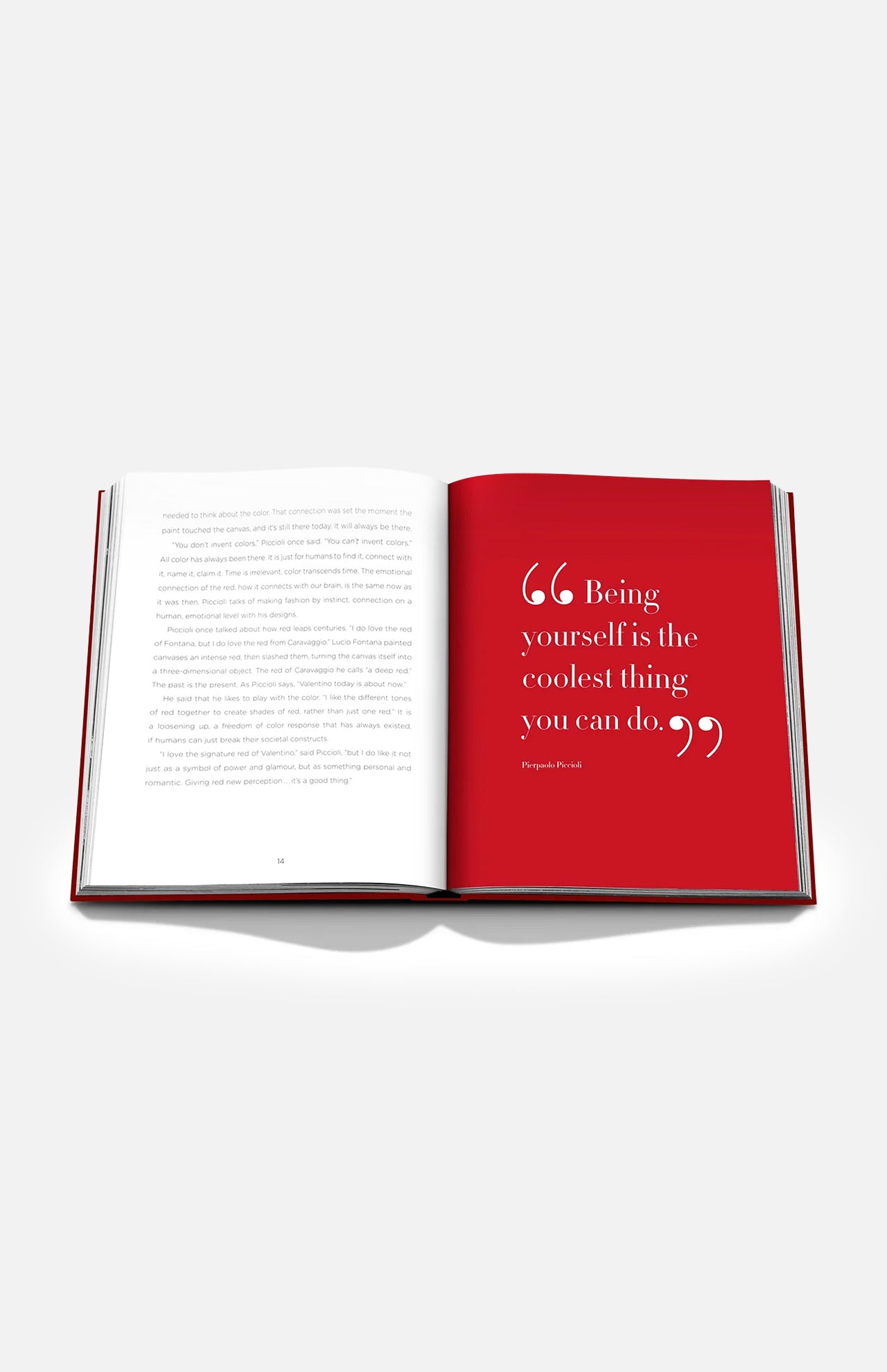 An open copy of ASSOULINE’s *Valentino Rosso* rests on a white surface, displaying one white page filled with text and one vivid red page—evocative of Rosso Valentino, the iconic shade celebrated in haute couture. The bold red page presents the quote: “Being yourself is the coolest thing you can do.”.