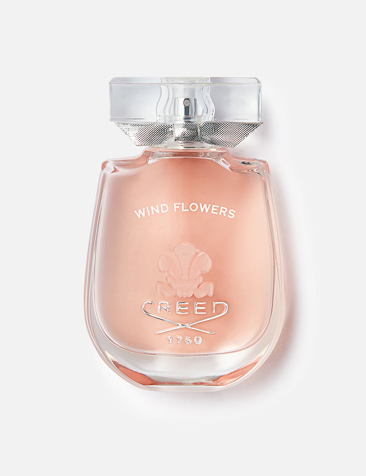 A clear glass bottle of Wind Flowers Fragrance by CREED, filled with pale pink liquid and topped with a silver cap, features jasmine and orange blossom notes; the brand name and logo are embossed on the front.