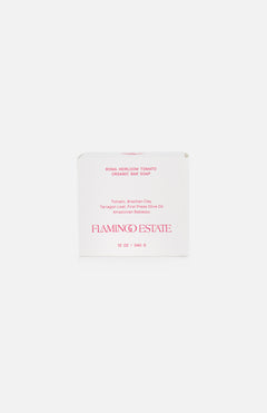 FLAMINGO ESTATE's Roma Heirloom Tomato Bar Soap comes in a white box with red text, highlighting nutrient-rich plant oils, Brazilian clay, and tarragon leaf. This 12 oz organic soap brings a fresh twist to your home fragrance routine.